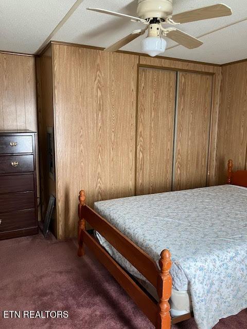 carpeted bedroom featuring wood walls and a ceiling fan
