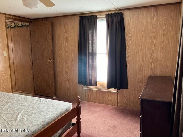 carpeted bedroom featuring wood walls, multiple windows, and a ceiling fan