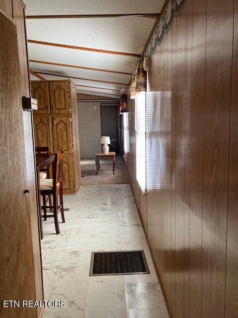 hallway with wooden walls, visible vents, lofted ceiling, and light floors