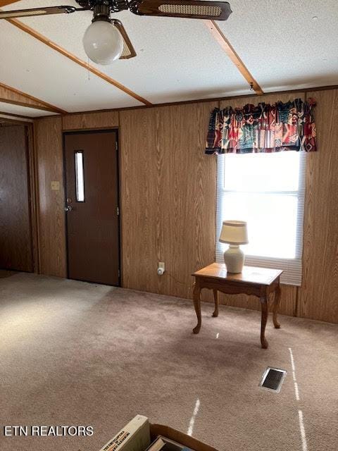 interior space featuring wooden walls, visible vents, a textured ceiling, and ceiling fan