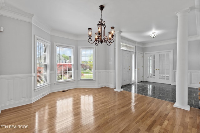 unfurnished dining area with a notable chandelier, a wainscoted wall, and ornate columns