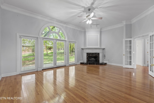 unfurnished living room featuring a high end fireplace, french doors, light wood-style floors, crown molding, and ceiling fan