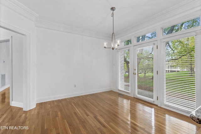 unfurnished dining area with wood finished floors, visible vents, ornamental molding, baseboards, and a notable chandelier