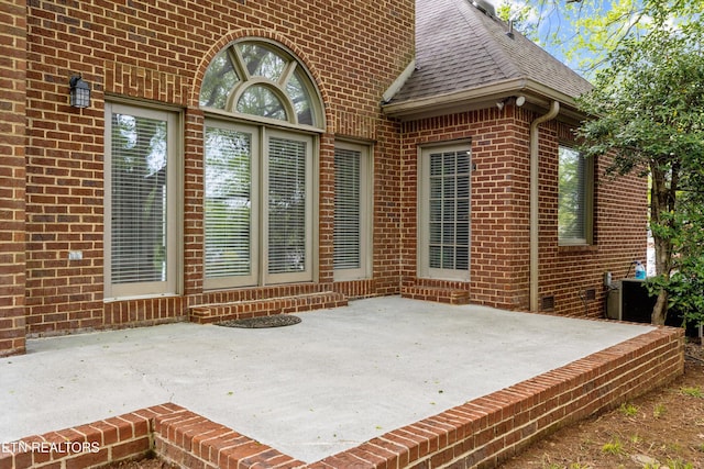 exterior space with a shingled roof, brick siding, and a patio