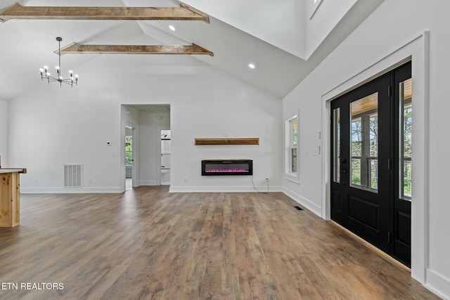 unfurnished living room with beam ceiling, high vaulted ceiling, a glass covered fireplace, wood finished floors, and visible vents