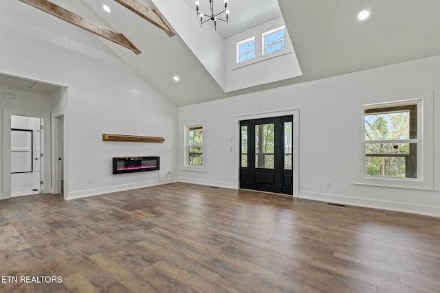 unfurnished living room featuring baseboards, a glass covered fireplace, a wealth of natural light, and high vaulted ceiling