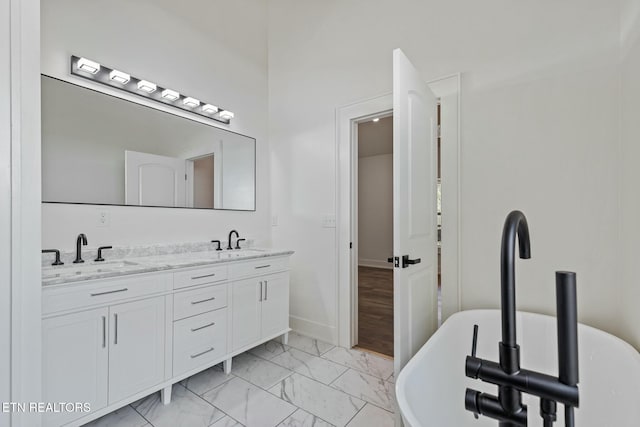 full bath featuring double vanity, a sink, a freestanding tub, and marble finish floor