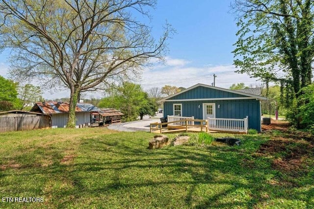 rear view of property featuring board and batten siding, a lawn, fence, and a deck