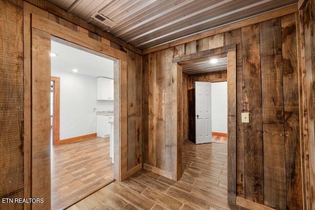hall featuring wood tiled floor, wooden walls, visible vents, and baseboards