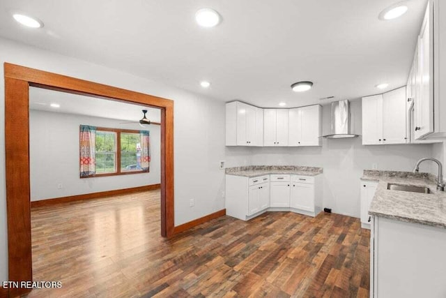 kitchen with wall chimney exhaust hood, a sink, dark wood-style floors, and baseboards