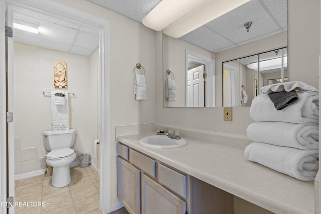 bathroom featuring tile patterned floors, a drop ceiling, toilet, vanity, and baseboards