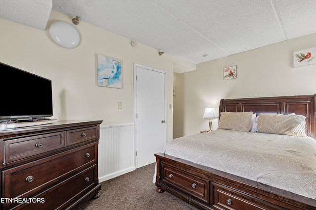 bedroom with dark colored carpet, a textured ceiling, and wainscoting