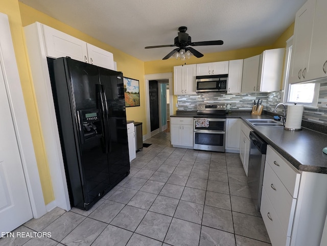 kitchen featuring backsplash, dark countertops, white cabinets, stainless steel appliances, and a sink