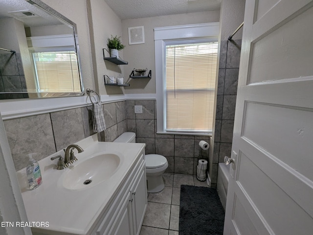 full bathroom with vanity, tile patterned flooring, a textured ceiling, toilet, and tile walls