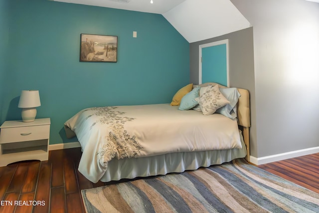 bedroom with vaulted ceiling, wood finished floors, and baseboards