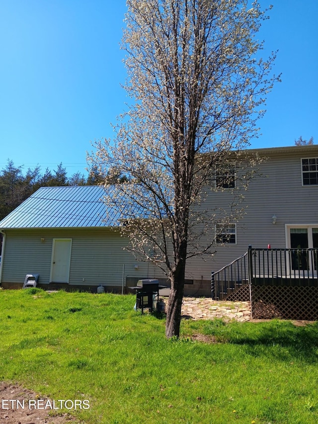 rear view of house featuring a lawn, a deck, and metal roof