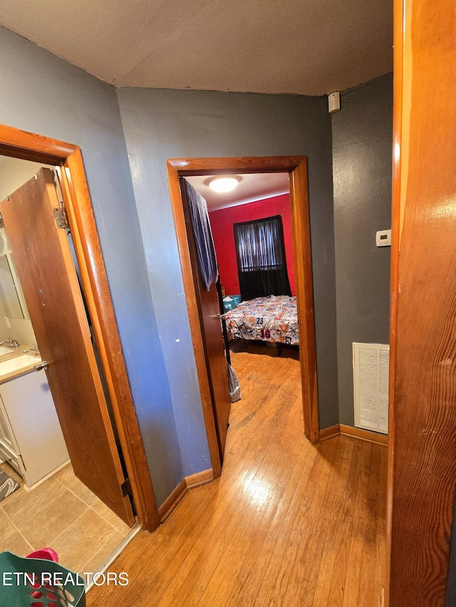 hall featuring visible vents, baseboards, and light wood-style flooring
