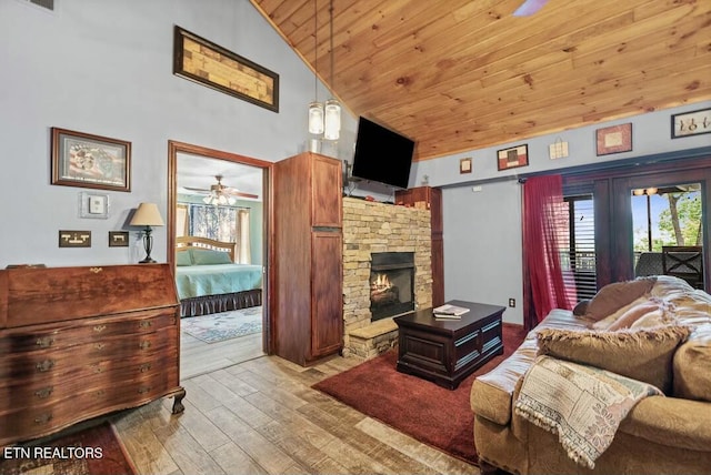 living area with wooden ceiling, a stone fireplace, ceiling fan, light wood-style floors, and high vaulted ceiling