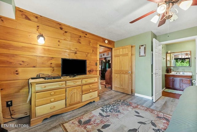 bedroom featuring baseboards, ensuite bath, wooden walls, a ceiling fan, and wood finished floors