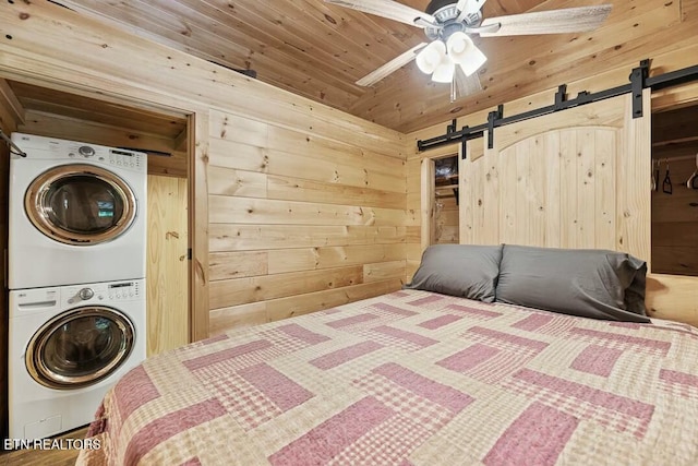 bedroom with wood walls, stacked washer / dryer, and a barn door