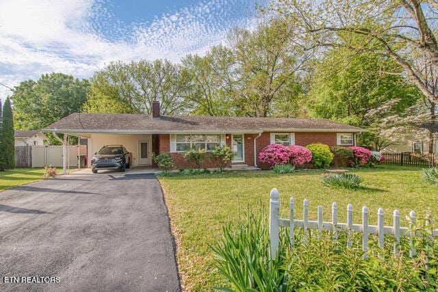 ranch-style home with driveway, fence, a carport, and a front yard