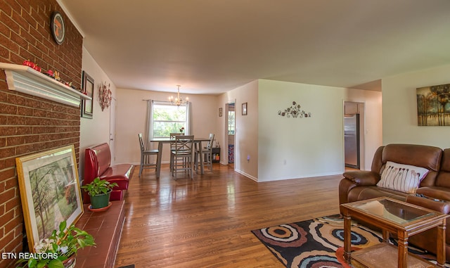 living room featuring baseboards, wood finished floors, a chandelier, and a brick fireplace