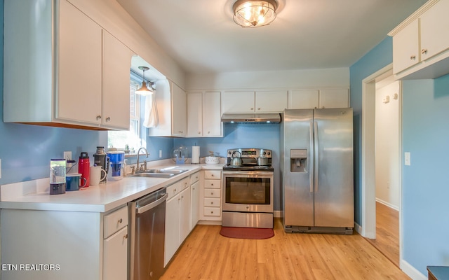 kitchen featuring stainless steel appliances, under cabinet range hood, a sink, and light wood-style floors