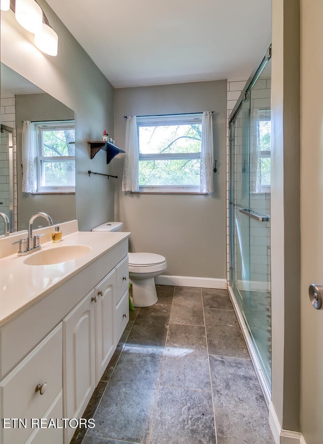 bathroom with toilet, a stall shower, baseboards, stone finish floor, and vanity
