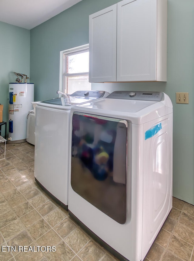 laundry area featuring washing machine and dryer, cabinet space, electric water heater, and stone finish flooring