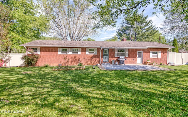 back of house featuring a chimney, fence, brick siding, a patio area, and a lawn