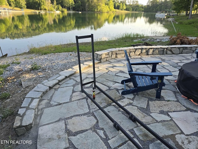 view of patio / terrace featuring a view of trees, a water view, and a grill
