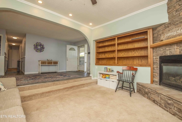 carpeted living room with arched walkways, a textured ceiling, ornamental molding, a stone fireplace, and recessed lighting