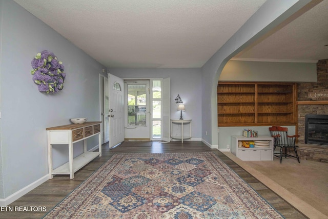 entryway with a textured ceiling, a fireplace, baseboards, and arched walkways