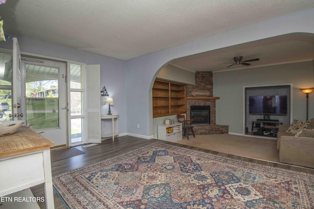 living room with baseboards, a fireplace, a textured ceiling, ceiling fan, and arched walkways