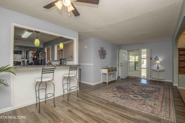 kitchen featuring a kitchen breakfast bar, a textured ceiling, a ceiling fan, black fridge with ice dispenser, and wood finished floors