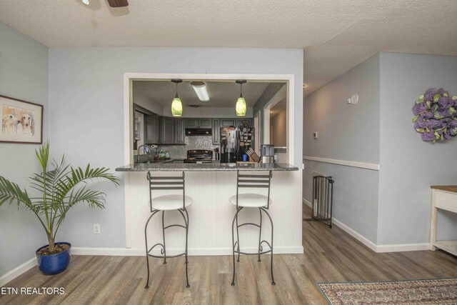 kitchen featuring a kitchen breakfast bar, under cabinet range hood, range with electric stovetop, decorative backsplash, and wood finished floors