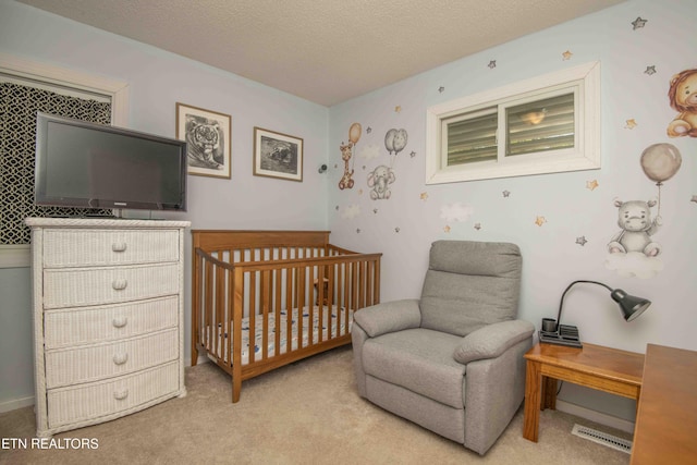 bedroom with a crib, visible vents, light colored carpet, and a textured ceiling