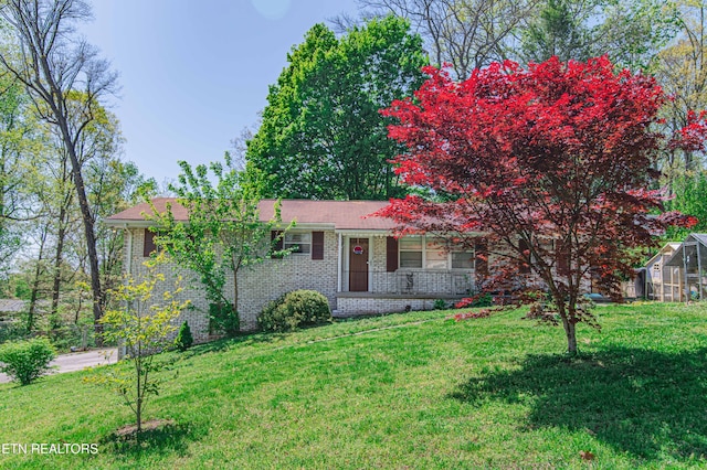 view of front of property with a porch, brick siding, a greenhouse, and a front lawn