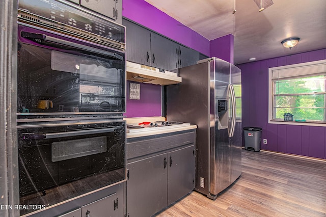 kitchen with light wood-style floors, dobule oven black, stainless steel fridge with ice dispenser, white stovetop, and under cabinet range hood
