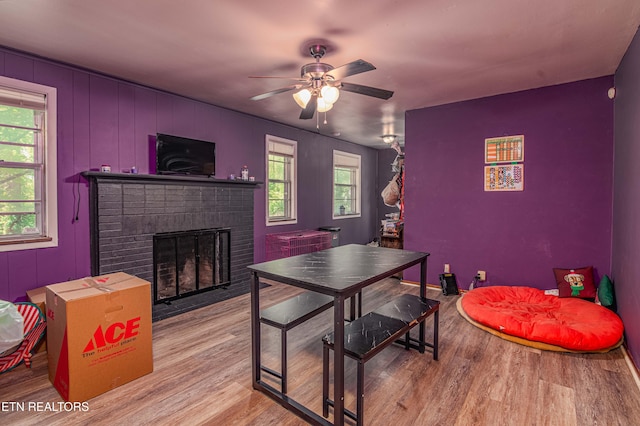 dining room featuring a brick fireplace, a ceiling fan, wood finished floors, and a healthy amount of sunlight