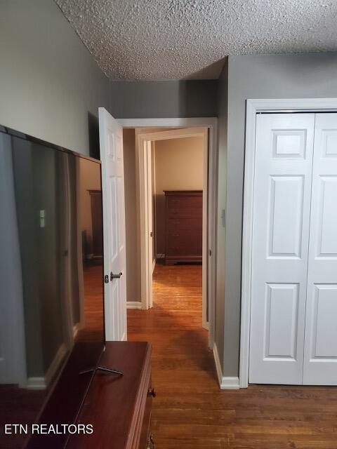 hallway featuring dark wood-style floors, a textured ceiling, and baseboards