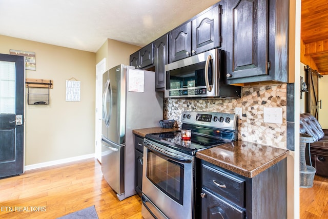 kitchen featuring appliances with stainless steel finishes, dark countertops, tasteful backsplash, and light wood-style flooring