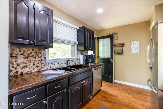 kitchen featuring dark countertops, a sink, light wood-style flooring, and stainless steel appliances