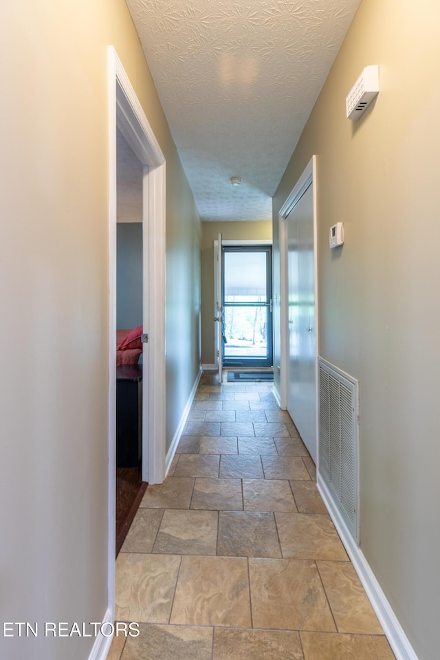 hallway with visible vents, stone tile floors, a textured ceiling, and baseboards