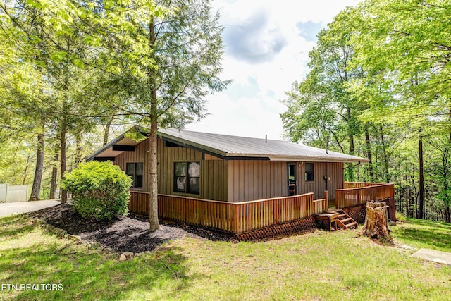 back of property with metal roof, a wooden deck, and a yard