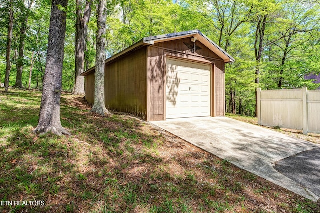 detached garage featuring concrete driveway and fence