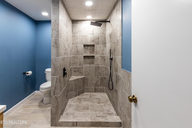 bathroom with recessed lighting, wood finished floors, a tile shower, toilet, and baseboards