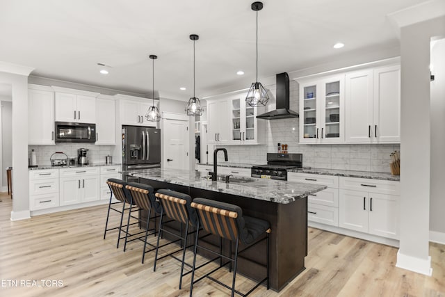 kitchen featuring light wood finished floors, a sink, gas range, and wall chimney range hood