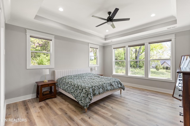 bedroom with light wood-style flooring, visible vents, a raised ceiling, and multiple windows