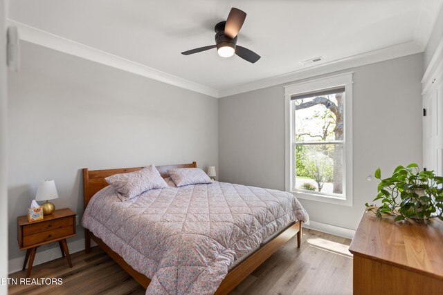 bedroom with wood finished floors, visible vents, ornamental molding, and multiple windows